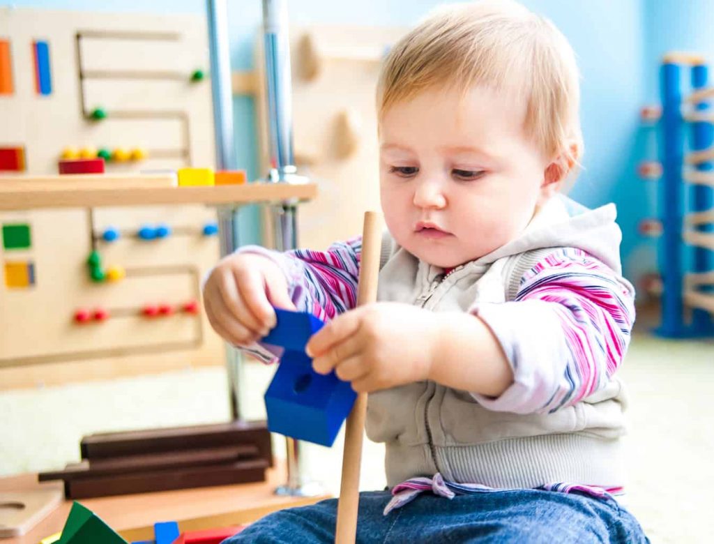 Cute little girl in the classroom early development plays with numerous  toys